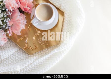Tasse de café blanc et décorations sur un plateau doré de style nordique. Pivoines roses. Un tissu écossais blanc se trouve sur un canapé en cuir. Banque D'Images