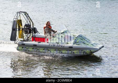 Homme en uniforme de camouflage et gilet de sauvetage à bord d'un hydroglisseur le long de la surface de l'eau. Un bateau pneumatique gonflable en caoutchouc navigue sur la rivière à vitesse élevée Banque D'Images