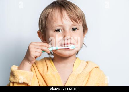 Mignonne heureuse adorable petite fille vêtue de peignoir jaune se brossant les dents. Banque D'Images