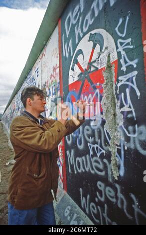 Un homme de l'Allemagne de l'Ouest utilise un marteau et un burin pour chip off un morceau du Mur de Berlin comme souvenir. Une partie du mur a déjà été démolis sur la Potsdamer Platz. Banque D'Images