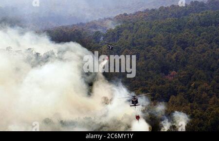 Deux hélicoptères Blackhawks UH-60 de la Garde nationale du Texas survolent les flammes pour évacuer l'eau des seaux de livraison d'eau de lutte contre les incendies aériens. Les équipes de la Garde nationale du Texas ont été lancées à partir de l'installation aérienne de l'armée d'Austin pour combattre les incendies de forêt menaçant les maisons et les biens près de Bastrop, au Texas, le 6 septembre 2011. Depuis 1975, le Département de l'agriculture et le Département de l'intérieur des États-Unis ont conclu un accord interagences avec le Département de la défense (DOD) qui permet au Département de fournir un soutien en matière de lutte contre les incendies aux agences de gestion des incendies de forêt, au besoin. Depuis 1975, le département américain d'Agricult Banque D'Images