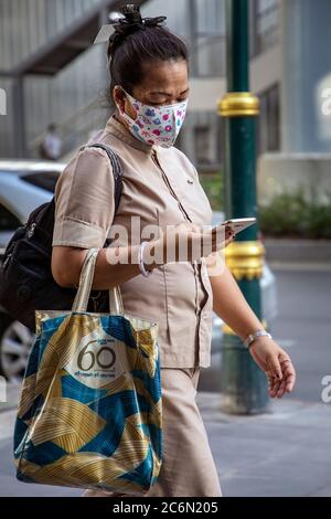 Femme portant un masque facial utilisant un téléphone portable pendant la pandémie Covid 19, Sukhumvit, Bangkok, Thaïlande Banque D'Images