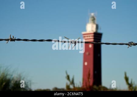 Phare Ouddorp, tour rouge avec sommet blanc, ciel bleu. Fil barbelé au premier plan. Pays-Bas Banque D'Images