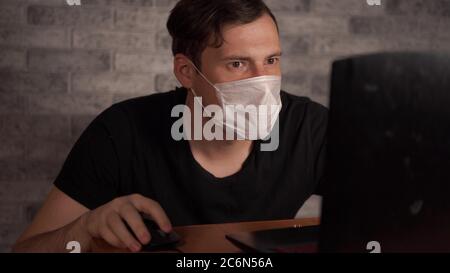 Un homme dans un masque médical apprend des nouvelles sur le coronavirus de l'Internet à l'aide d'un ordinateur portable. L'homme est préoccupé par sa santé. L'épidémie de Banque D'Images
