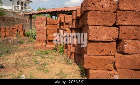 Piles de briques dans la cour. Des briques rouges en sorge empilées sur un sol sablonneux avec de l'herbe le jour ensoleillé dans la cour Banque D'Images