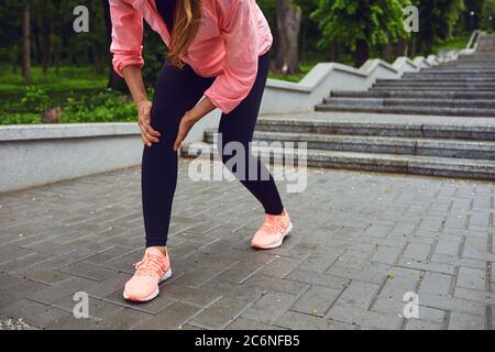 Coureur méconnaissable souffrant de douleurs au genou pendant l'entraînement matinal au parc. Jogger souffrant de blessures sportives Banque D'Images