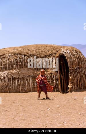 Serengeti, Tanzanie - septembre 21. 2012: Un jeune garçon Massai souriant en rouge devant les huttes traditionnelles à l'intérieur d'un village Massai dans le Serenget Banque D'Images