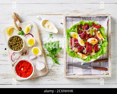 salade de poulpes avec œufs durs, câpres, oignon mariné sur feuilles de laitue dans un bol sur un plateau, sur une table rustique en bois avec ingrédients, fl Banque D'Images