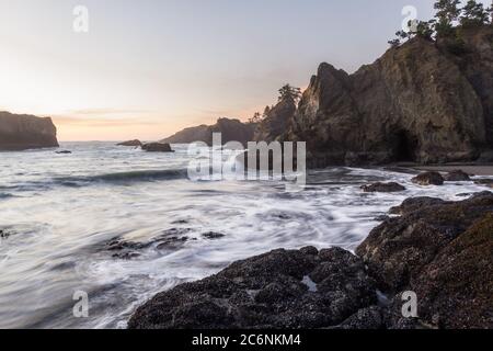 Le soleil se couche sur Secret Beach, sur la côte sud de l'Oregon, au coucher du soleil, avec ses nombreux îlots recouverts d'arbres à feuilles persistantes et de vagues floues qui se déplacent vers l'intérieur Banque D'Images