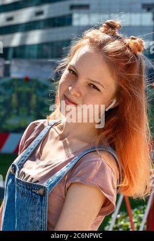 portrait d'une belle fille aux cheveux rouges avec des taches de rousseur lors d'une journée ensoleillée en ville avec des écouteurs Banque D'Images