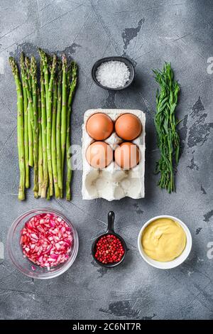 Asperges avec œufs et ingrédients de la vinaigrette française avec moutarde de dijon, oignon haché dans l'estragon au vinaigre rouge sur fond texturé gris, vue du dessus. Banque D'Images