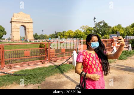 Une femme indienne debout devant l'emblématique porte de l'Inde tout en portant des masques de protection Corona prend un selfie Banque D'Images