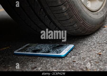 L'écran du smartphone est fissuré à plat sur la route, car le déplacement d'un pneu de voiture à l'avant et à l'arrière-plan est flou Banque D'Images