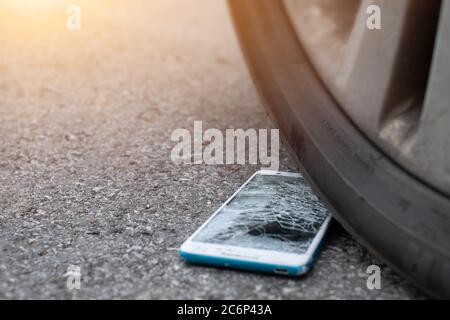 L'écran du smartphone est fissuré à plat sur la route, car le déplacement d'un pneu de voiture à l'avant et à l'arrière-plan est flou Banque D'Images