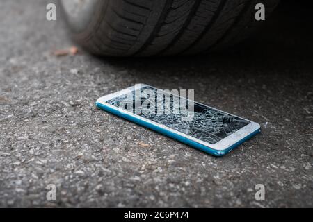 L'écran du smartphone est fissuré à plat sur la route, car le déplacement d'un pneu de voiture à l'avant et à l'arrière-plan est flou Banque D'Images
