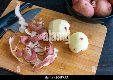 Épluchage des pommes de terre rouges sur une planche à découper en bambou : pommes de terre crues avec un éplucheur de légumes et un couteau de cuisine sur une planche à découper en bois Banque D'Images