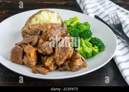 Diane Casserole avec accompagnements : morceaux de bœuf, oignons et champignons dans une sauce tomate, servis avec des fleurs de brocoli et une pomme de terre cuite au four Banque D'Images