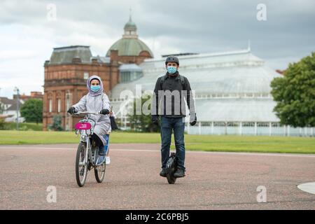 Glasgow, Écosse, Royaume-Uni. 11 juillet 2020. Photo : un couple est vu sur son vélo et un monocycle électrique portant des masques chirurgicaux bleus tandis qu'ils apprécient l'air de l'après-midi à Glasgow Green pendant le verrouillage facilité. Comme les scooters électriques sont maintenant la norme, les monocycles électriques vont-ils s'accrocher? Crédit : Colin Fisher/Alay Live News Banque D'Images