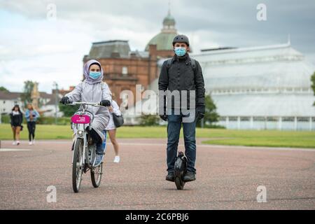 Glasgow, Écosse, Royaume-Uni. 11 juillet 2020. Photo : un couple est vu sur son vélo et un monocycle électrique portant des masques chirurgicaux bleus tandis qu'ils apprécient l'air de l'après-midi à Glasgow Green pendant le verrouillage facilité. Comme les scooters électriques sont maintenant la norme, les monocycles électriques vont-ils s'accrocher? Crédit : Colin Fisher/Alay Live News Banque D'Images