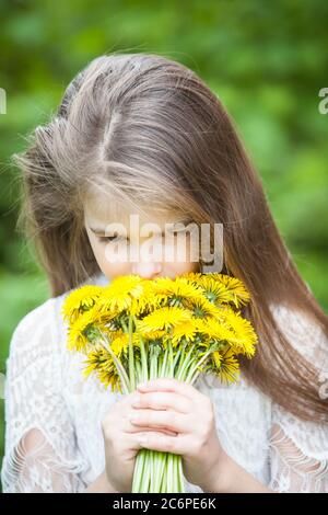 fille à la mode dans une robe légère pose et tient un grand bouquet de pissenlits jaunes Banque D'Images