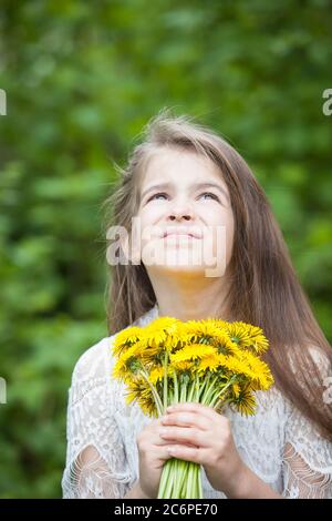 fille à la mode dans une robe légère pose et tient un grand bouquet de pissenlits jaunes Banque D'Images