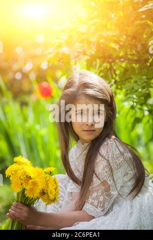 fille à la mode dans une robe légère pose et tient un grand bouquet de pissenlits jaunes Banque D'Images