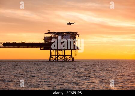 Une installation en mer avec un hélicoptère a atterri sur elle pendant le coucher du soleil Banque D'Images
