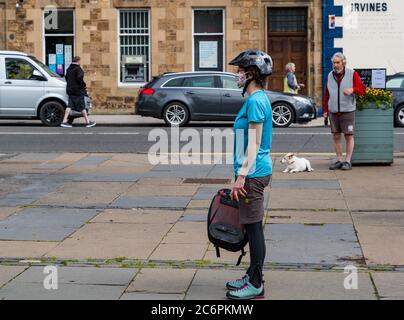 Femme cycliste portant un masque facial et un casque de vélo en file d'attente pour Farmers Market pendant la pandémie Covid-19, Haddington, East Lothian, Écosse, Royaume-Uni Banque D'Images