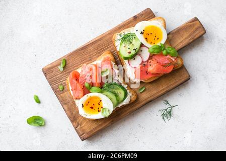 Sandwich au saumon ouvert sain avec fromage à la crème, œuf mou, légumes et légumes verts. Délicieux sandwich de poisson aux protéines pour le petit déjeuner ou le brunch. Banque D'Images