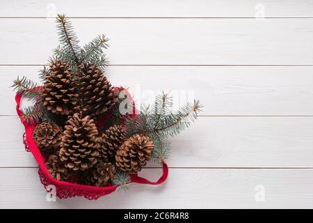 Sac en coton rouge en maille avec branches et cônes en sapin de Noël sur panneau en bois. Aucun gaspillage. Noël écologique. Vue d'en haut. Copier l'espace. Banque D'Images