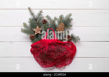 Sac en coton rouge en maille avec branches et cônes en sapin de Noël sur panneau en bois. Aucun gaspillage. Noël écologique. Vue d'en haut. Banque D'Images