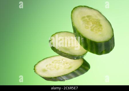 Trois morceaux de concombre pendent arbitrairement sur un fond vert avec un gradient. Banque D'Images