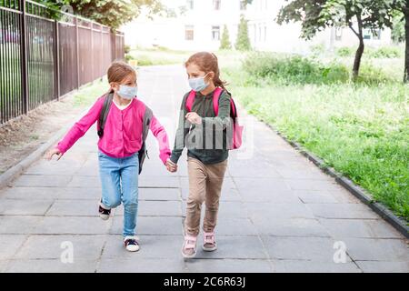 Deux filles qui reviennent à l'école pendant une pandémie de coronavirus. Élèves de l'école primaire avec des sacs d'école portant un masque facial de protection allant à l'école. Banque D'Images