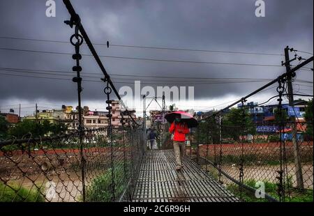 Katmandou, Népal. 10 juillet 2020. Un népalais marche sous un parapluie sur le pont au-dessus de la rivière Bishnunati après de fortes pluies à Katmandou. Les fortes pluies laissent les népalais exposés à des inondations et à des glissements de terrain pendant la saison de la mousson. Crédit : Sunil Sharma/ZUMA Wire/Alay Live News Banque D'Images