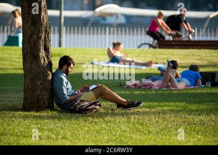 Un jeune homme barbu lit assis sur l'herbe dans un parc Banque D'Images