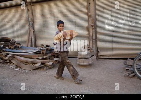 Un garçon afghan qui travaille comme assistant dans un atelier d'automobile, transporte du pain fraîchement cuit pour ses collègues, dans le quartier de Pia Minara, dans la ville de Herat, au nord-ouest. L'afghan moyen lutte pour soutenir sa famille à hauteur de 3 dollars par jour et environ 20 à 30 % des enfants en âge d'aller à l'école primaire travaillent pour compléter le revenu familial. Des milliers d'enfants travaillent dans des conditions dangereuses dans tout l'Afghanistan. 20 juin 2007. Banque D'Images