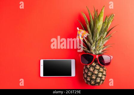 Célébrez le concept de la Journée des ananas d'été, vue du dessus de l'ananas drôle porter des lunettes de soleil rouges et smartphone écran vierge, isolé sur fond rouge, Holid Banque D'Images