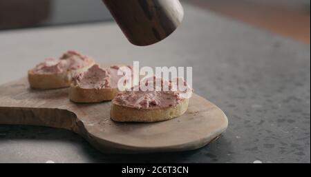 l'homme moudre le poivre noir frais sur la pâte de viande bruschettas on bois Banque D'Images