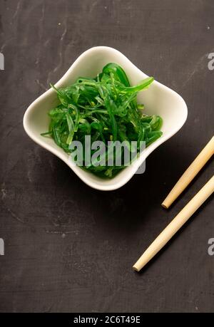 Sélection sélective, salade de Chuka de mer aux graines de sésame dans des plats en céramique blanche, avec des bâtonnets de bambou sur fond sombre Banque D'Images