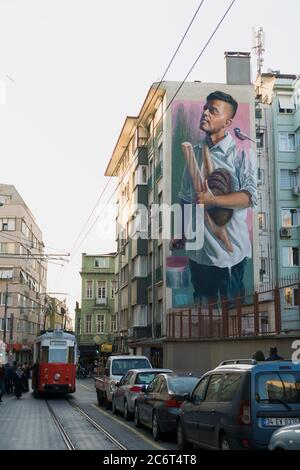 Istanbul, Turquie - 23 février 2020 : un grand art mural d'un jeune homme tient des pains à Istanbul Moda. Un tramway nostalgique attend les passagers à Banque D'Images