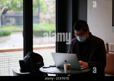 Le coronavirus COVID-19 a été contrôlé en Chine. Un homme portant un masque chirurgical travaillant dans un café Banque D'Images