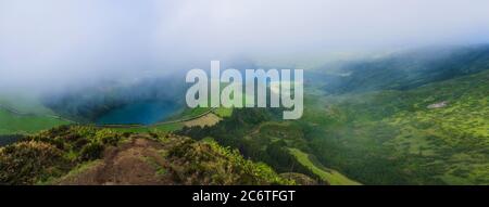 Vue panoramique sur les lacs volcaniques. Vert Lagoa de Santiago et bleu Lagoa Azul avec Sete Cidades village, partiellement couvert de brouillard et cl Banque D'Images