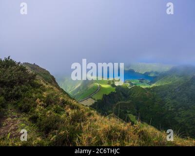 Vue imprenable sur les lacs volcaniques. Vert Lagoa de Santiago et bleu Lagoa Azul avec le village de Sete Cidades, partiellement couvert de brouillard et de nuages. Sao Banque D'Images