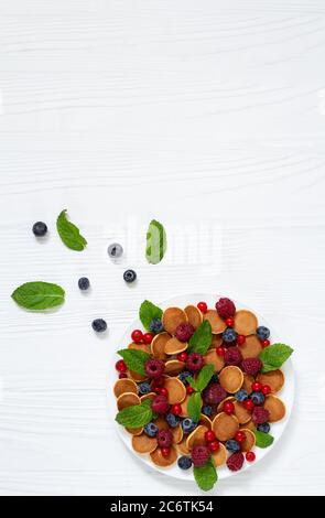 Petit déjeuner d'été sain avec de minuscules crêpes, baies fraîches et feuilles de menthe vue sur la table en bois blanc Banque D'Images