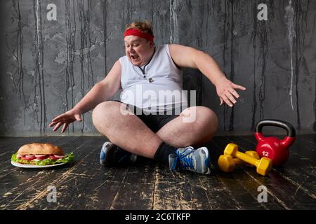 obèse jeune homme caucasien empiète sur un gros sandwich, l'homme gras ne peut pas adhérer à un mode de vie sain et à une alimentation Banque D'Images