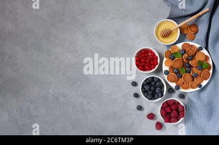 Dessert tendance et petit déjeuner sain. Céréales à crêpes ou mini crêpes au miel, baies fraîches sur ardoise vue de dessus. Espace pour votre texte Banque D'Images