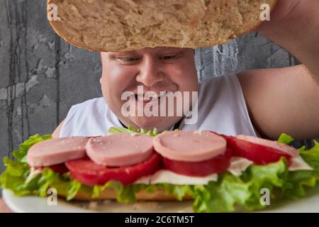 comic caucasien embonpoint homme ouvre à l'intérieur de sandwich, regarde les ingrédients. nutrition, malsain concept de style de vie Banque D'Images