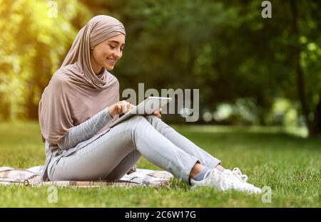 Jeune femme musulmane utilisant une tablette numérique au parc Banque D'Images