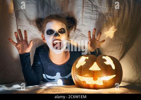 Joyeux Halloween ! Jolie petite fille en costume squelette avec une citrouille. Enfant s'amuser à la maison. Banque D'Images