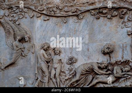 Dieu met le premier homme, Adam, à dormir, puis prend une côte de son côté pour créer la première femme, Ève, dans la Bible hébraïque des années 1300 / bas-relief en marbre de l'ancien Testament sur la façade ouest de la cathédrale d'Orvieto, Ombrie, Italie. Cette scène sculptée est attribuée à Lorenzo Maitani (c. 1275 - 1330), qui a conçu la façade gothique tardive de la cathédrale. Maitani aurait eu une contribution directe en tant que sculpteur sur deux panneaux couvrant deux des quatre pilastres inférieurs de la façade : un panneau de Maitani représente des scènes de la Bible hébraïque / ancien Testament, y compris la scène dans cette image. Banque D'Images